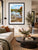 A framed landscape art print of a scenic river Dee in Llangollen with autumn foliage and a church spire, displayed on a beige wall in a modern living room setting.