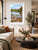 A framed landscape art print of a scenic river Dee in Llangollen with autumn foliage and a church spire, displayed on a beige wall in a modern living room setting.
