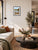 A framed landscape art print of a scenic river Dee in Llangollen with autumn foliage and a church spire, displayed on a beige wall in a modern living room setting.