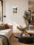 A framed landscape art print of a scenic river Dee in Llangollen with autumn foliage and a church spire, displayed on a beige wall in a modern living room setting.